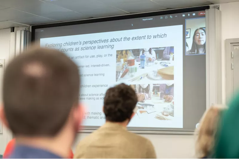 Photo of the big screen, showing Maia Yoshida, a past student, giving a remote presentation, at the Celebration event of the MA in STEM Education, in November 2021 at King's College London.