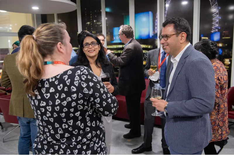 Three people, including two Indian people representing the WIPRO company, talking and laughing at the Celebration event of the MA in STEM Education, in November 2021 at King's College London.