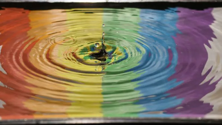 The colours of the LGBT flag (from left to right: red, orange, yellow, green, blue, purple and white) are showing over a pool of water.