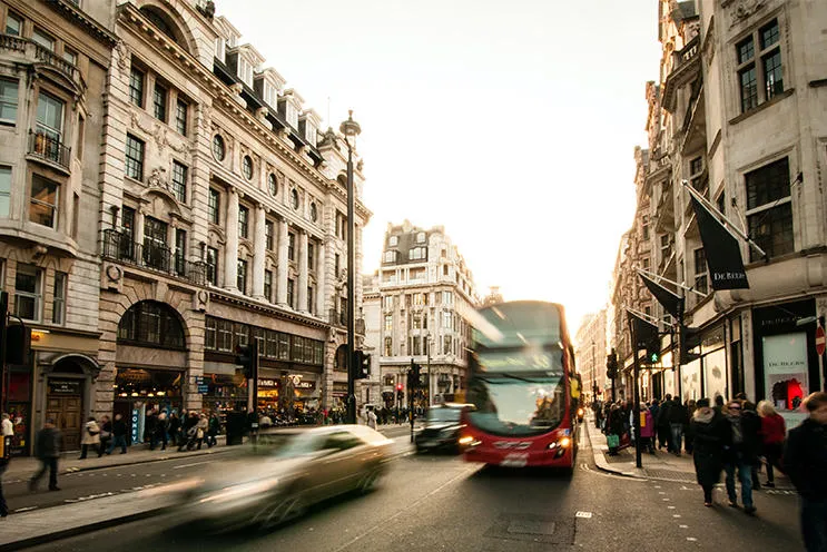 A london street with people walking and a red bus on the road