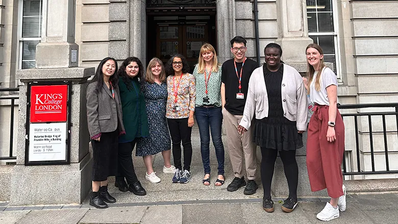 Dr Mili Mili and Dr Emma Towers in the middle of a group of student-researchers posing in front of Waterloo Bridge Wing entrance.