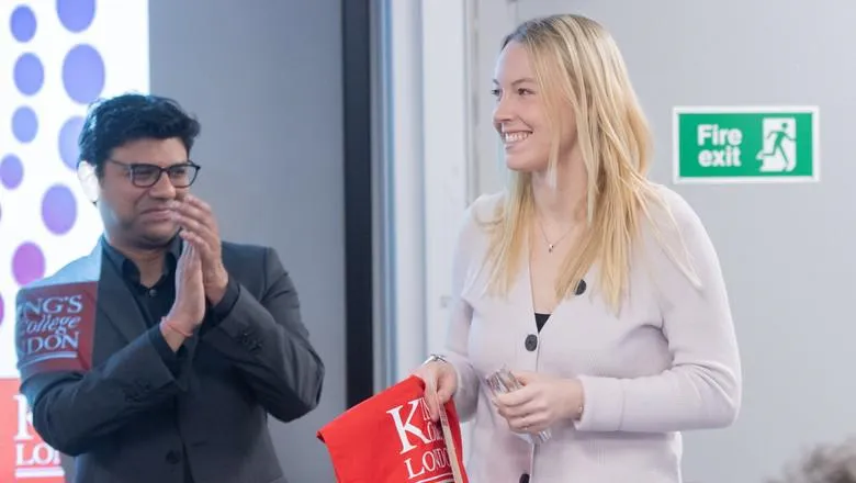 Natalie smiling after receiving the wipro award, next to a wipro representative clapping for her.