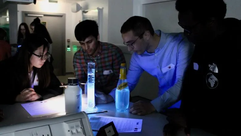 One female student with 3 male students doing an experiment with light in a darkened room.
