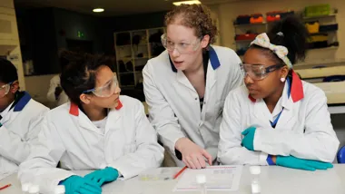 Two young students of colour in a lab with a science teacher