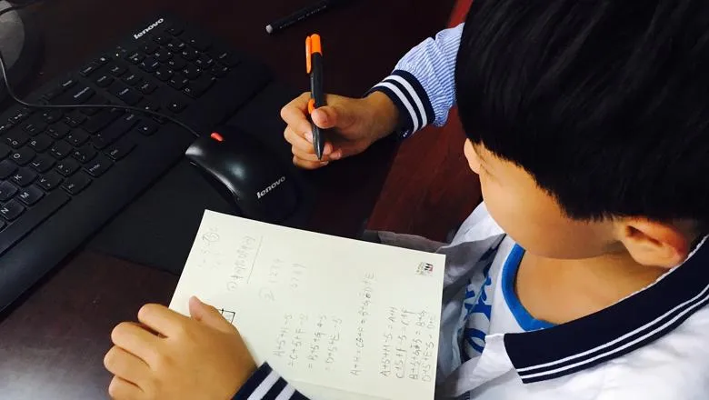 Child working at a computer with a pen and notepad