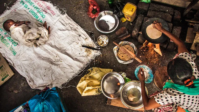 Baby sleeping on floor as mother cooks, India