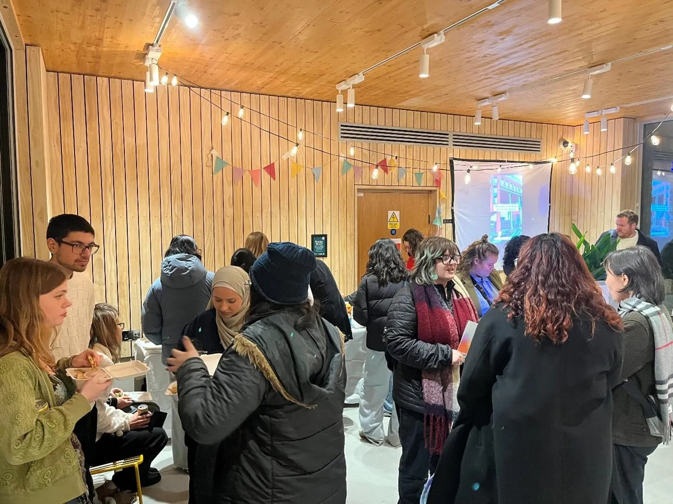 A group of attendees at the Cost of Learning Exhibition opening. Attendees are enjoying food, drink and are socialising.