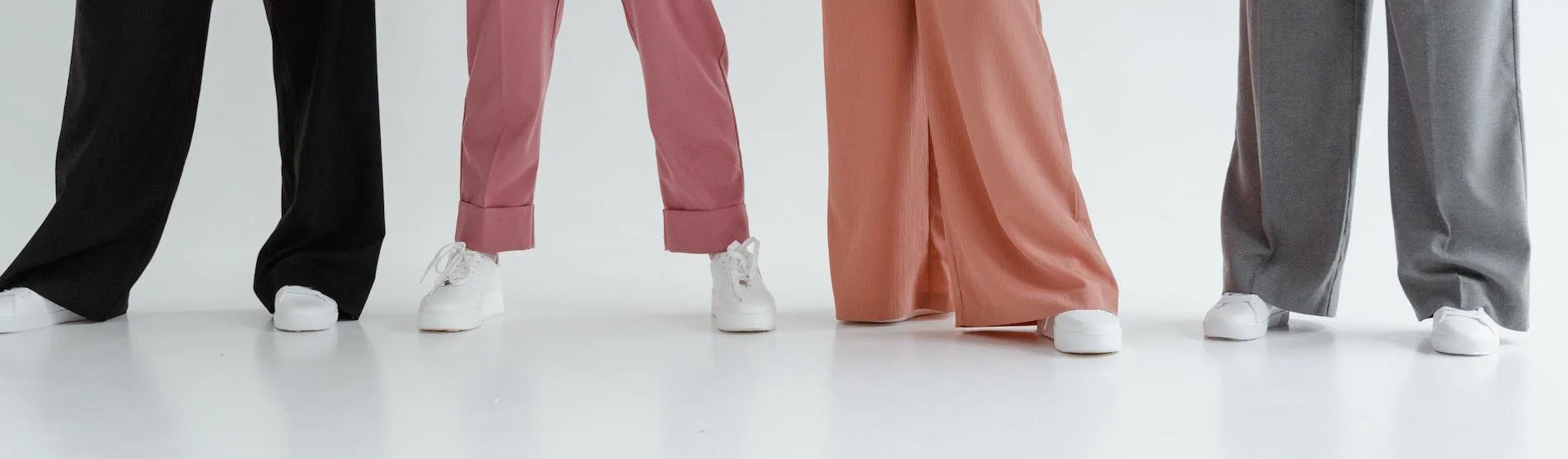 Four women wearing trousers and white trainers