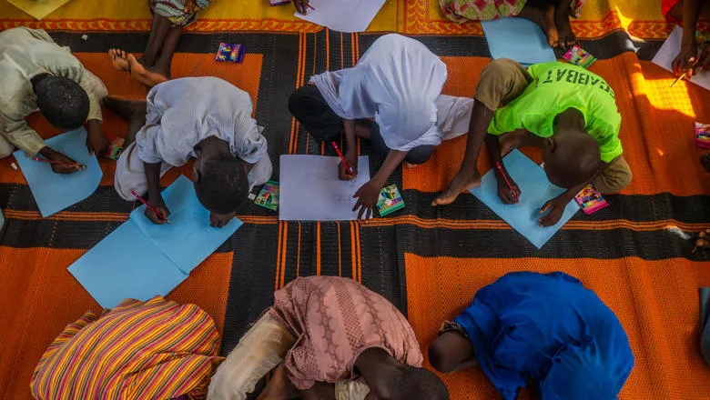Children sitting on a mat on the floor and drawing in Nigeria