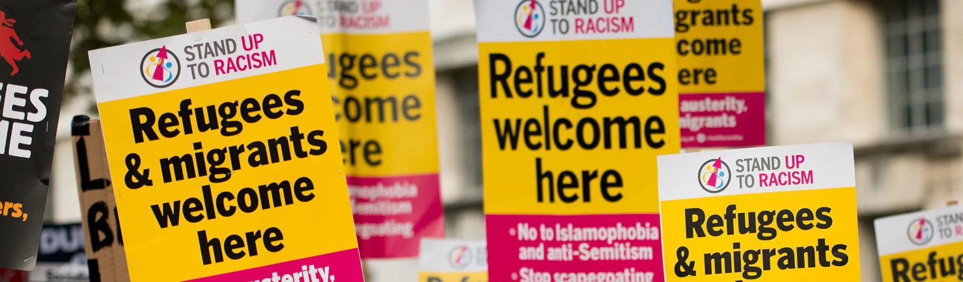 People at refugee protest holding 'refugees & migrants welcome here' signs