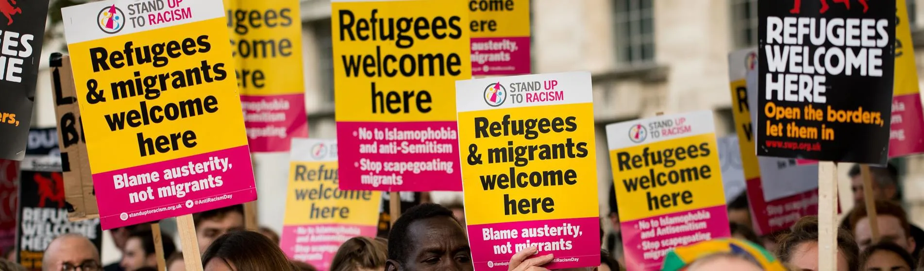 People at refugee protest holding 'refugees & migrants welcome here' signs