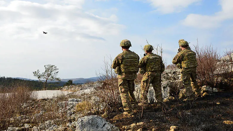 Soldiers looking out across a landscape with a plane in the sky.