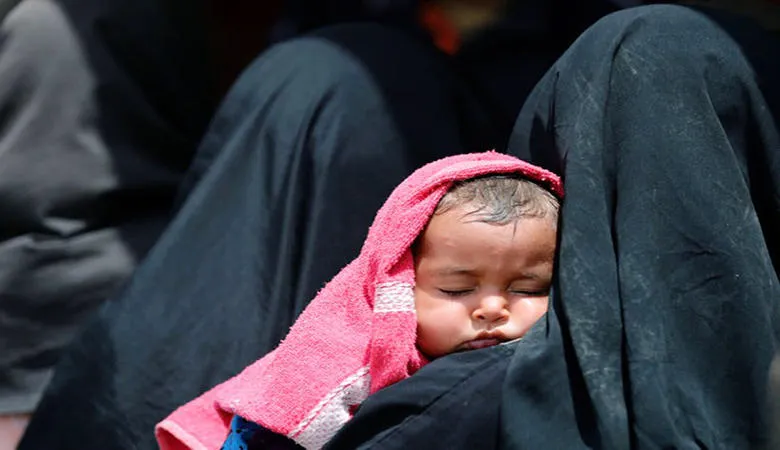 A woman in a headscarf holding a sleeping child