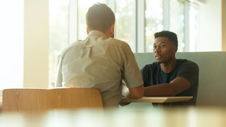 Two men sitting across a table in the sunshine