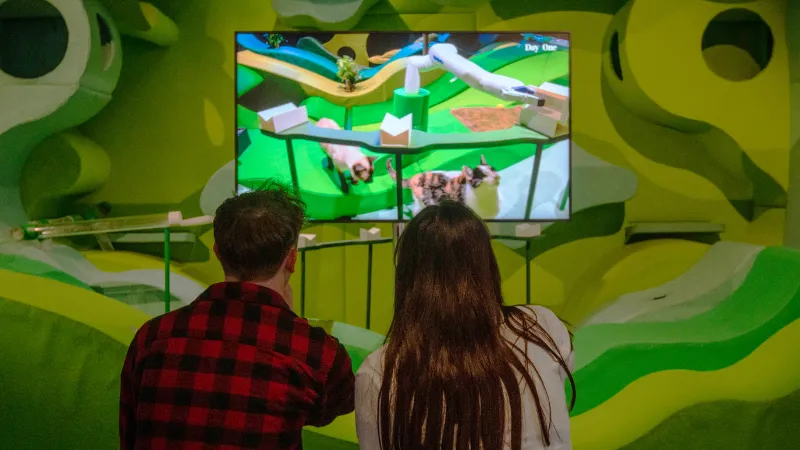 Two young people watching a video with vivid colours as part of the 'AI: Who's Looking After Me?' exhibition.