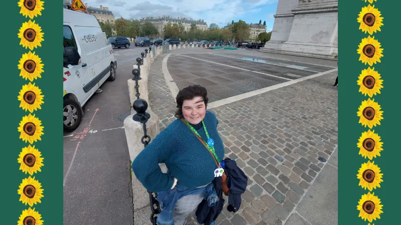 Alex wearing their Sunflower lanyard outside the Arc de Triomphe with a sunflower border
