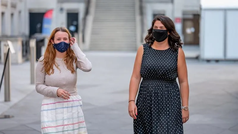 Two women smile behind face coverings while walking through the Bush House courtyard