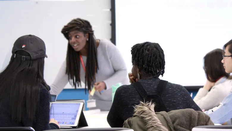 The backs of two students sitting down, looking at another person at the front of the room
