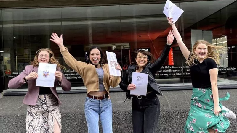 Four students jump in their air holding their dissertations in front of a sign that say's Kings College on Strand Campus