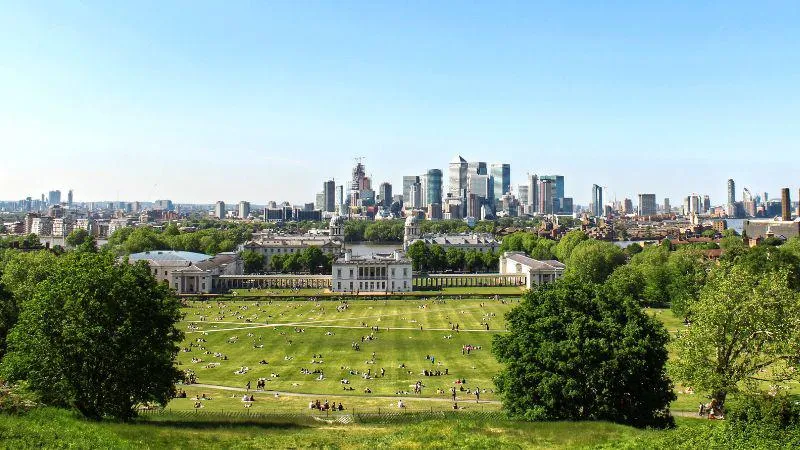 A photo from the top of the hill at Greenwich Park with the skyline of Canary Wharf and London in the background