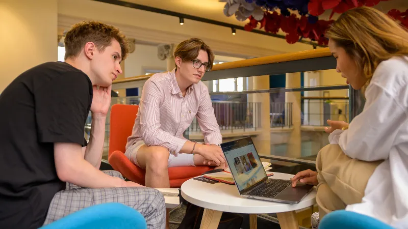 Three students preparing for a group presentation around a table and a laptop.