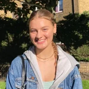 Isabel Lynch, a second-year English Language and Linguistics student, stands in a sunny garden wearing a light blue denim jacket and grey hoodie