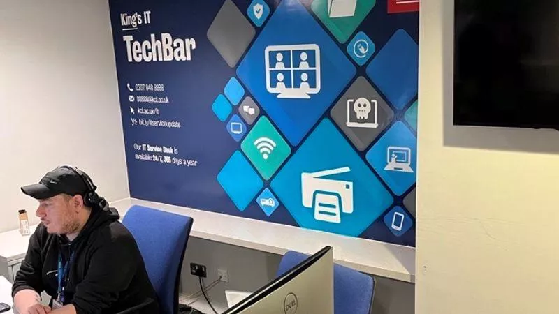 AN IT TEchbar table in a library with a blue and green banner behind it that says King's ITTechbar