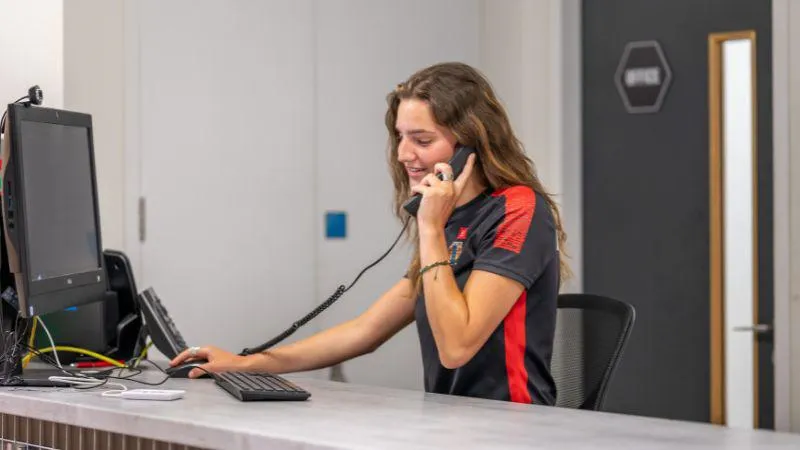 Image of a King's Sport & Wellness trainer answering the telephone at the reception desk of a gym