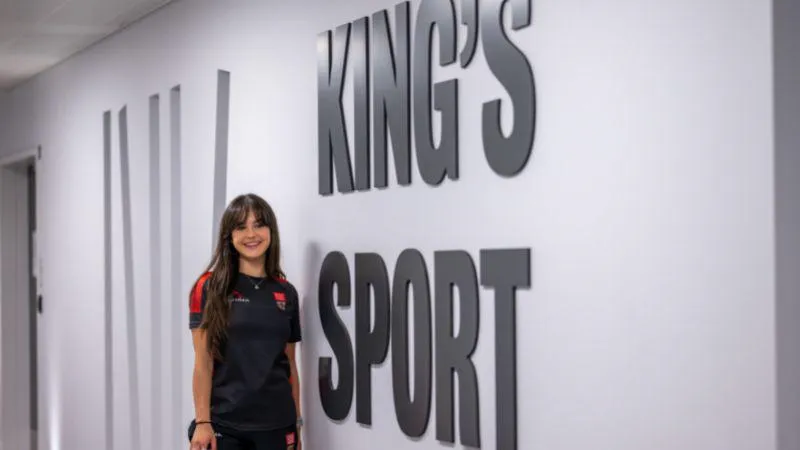 A King's Sport & Wellness trainer in front of a King's Sport wall sign