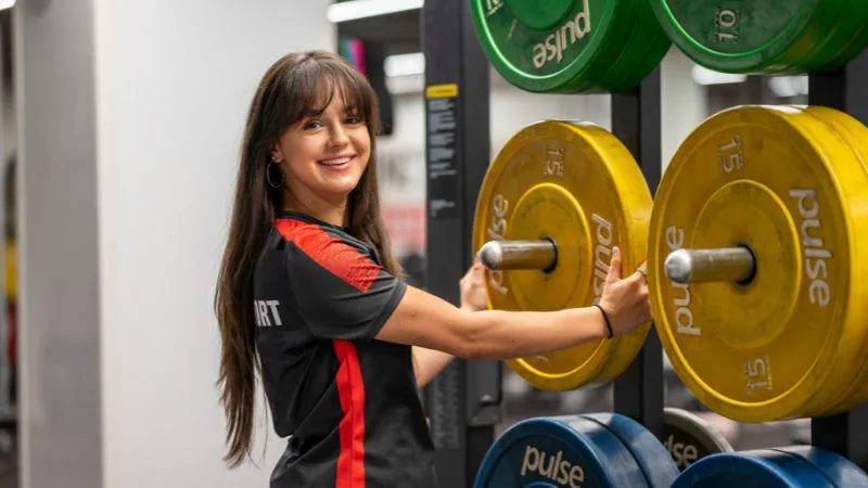 A King's Sport & Wellness trainer reracking weights in a gym