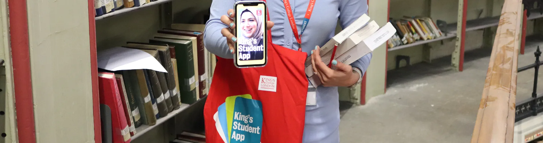 A student holding books and the King's Student App at the Maughan Library's Round Reading Room.