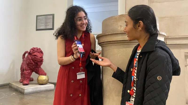 Two students talking about the app in front of Reggie's statue