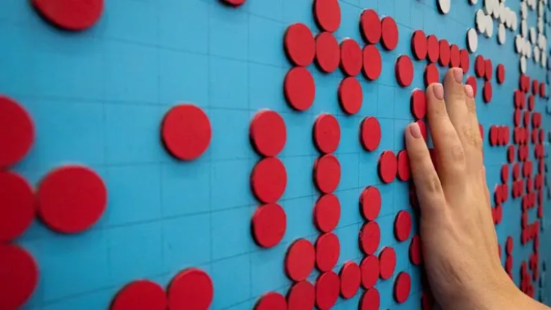An image of a hand touching a wall with small, three-dimensional red circles against a blue background