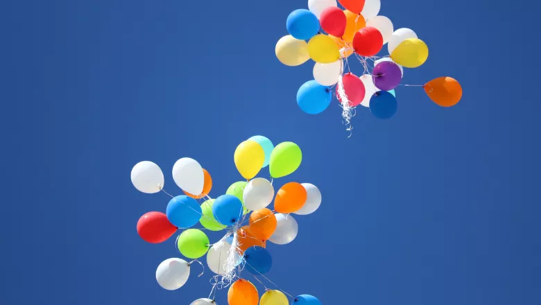 Two bunches of colourful balloons against a blue sky