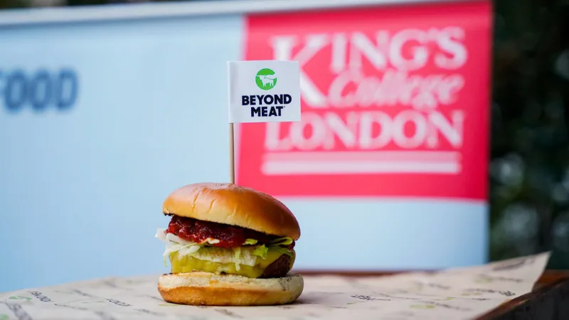 A Beyond Meat vegan burger with a Beyond Meat flag in the top, it is in front of a King's Food banner with the King's College London logo behind.