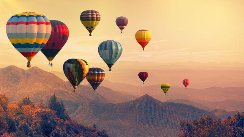 An image of hot air balloon rising above a mountain range with clouds.
