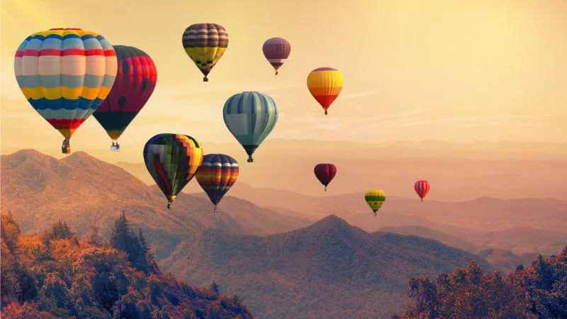 An image of hot air balloon rising above a mountain range with clouds.