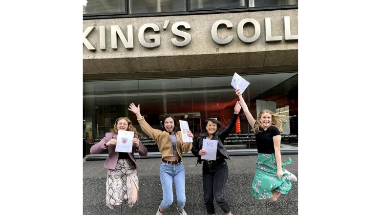 Four students jump in the air holding their dissertations in front of the King's building