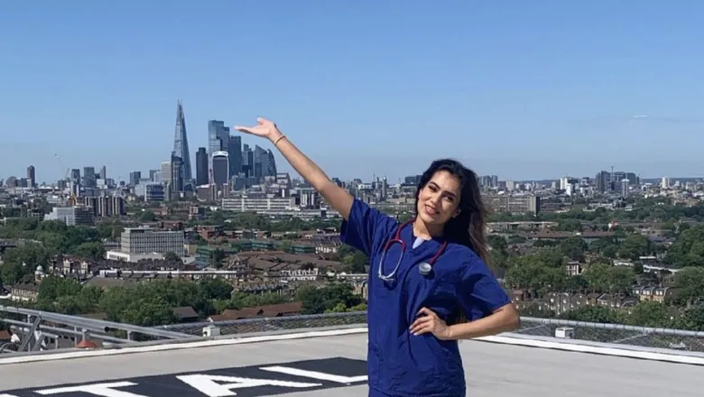 A student in blue scrubs on a rooftop with a view of the London skyline in the background