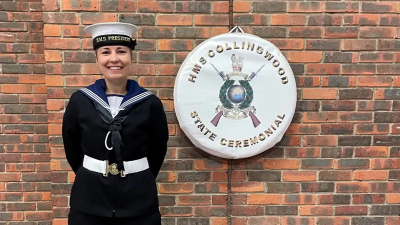 An image of Helen Vanson in Royal Navy uniform. She is stood in front of a ciricle banner saying, 'HMS Collingwood State Ceremonial'