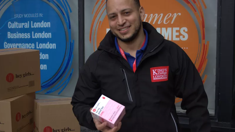 A member of King's Staff unpacking a delivery from Hey Girls, the man in the image is wearing a black King's zip up jacket with a pink and white Hey Girls product box.