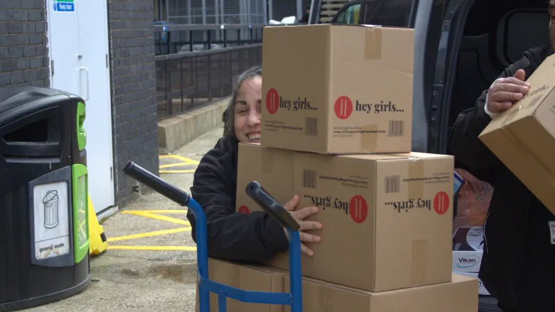 A smiling female member of King's staff holding on to a box from the Hey Girls delivery.
