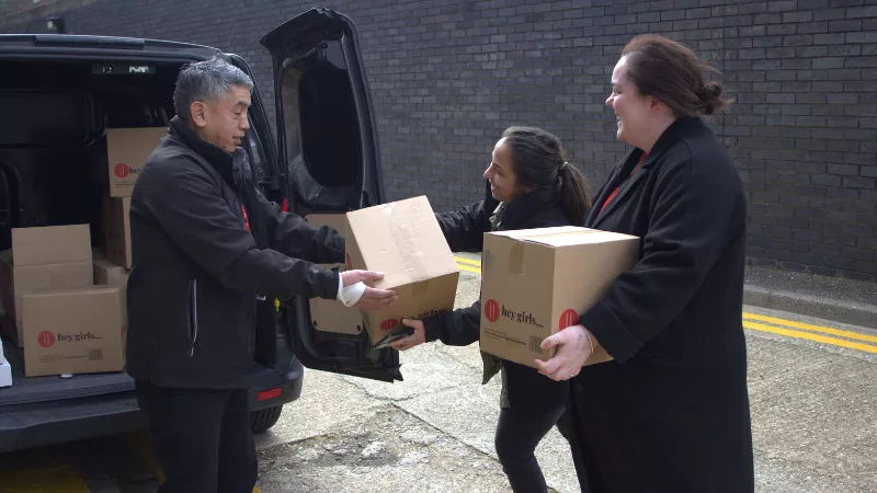 Three members of King's staff unload boxes from the back of a small black van.