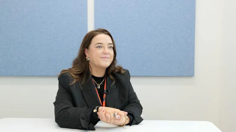 Smiling person sitting at table with hands clasped together