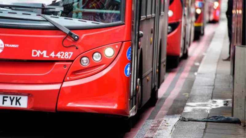 An image of four red London buses lined up ona. street with double red lines on the road.