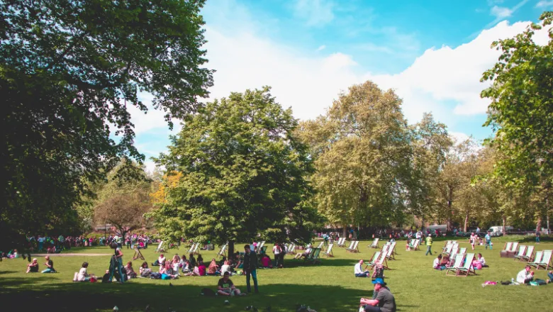 A London park in summer. People are sitting on the grass and on deckchairs