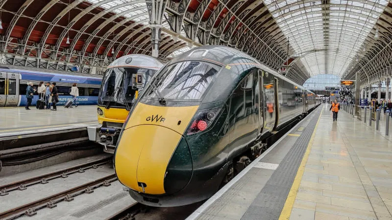 a green train in a victorian station with high, vaulted metal beamed roof