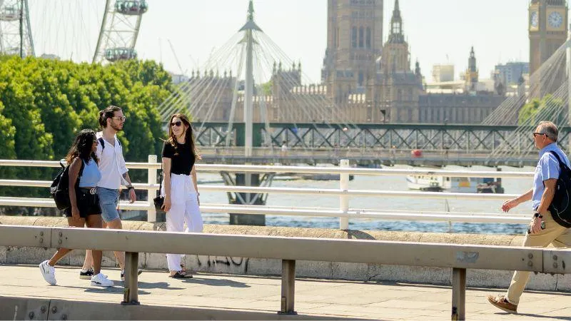 Three students walk along the Southbank on the River Thames with the Houses of parliament and a section of the London Eye in the background