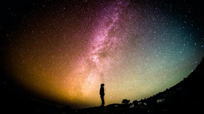 Silhouette of a person looking up at the colourful lights of the galaxy