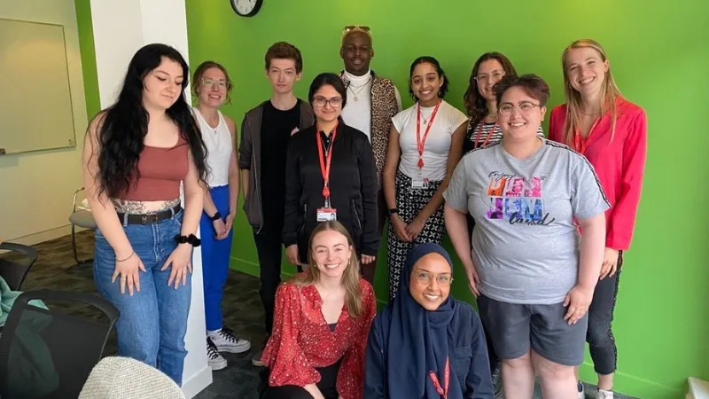 A group of King's students and members of staff posing and smiling in a room with a green wall.